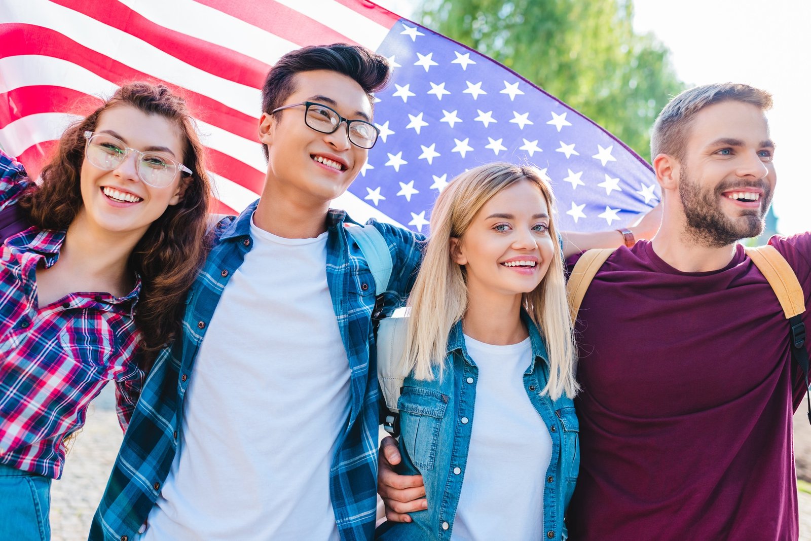 portrait of smiling multicultural students with american flag in park